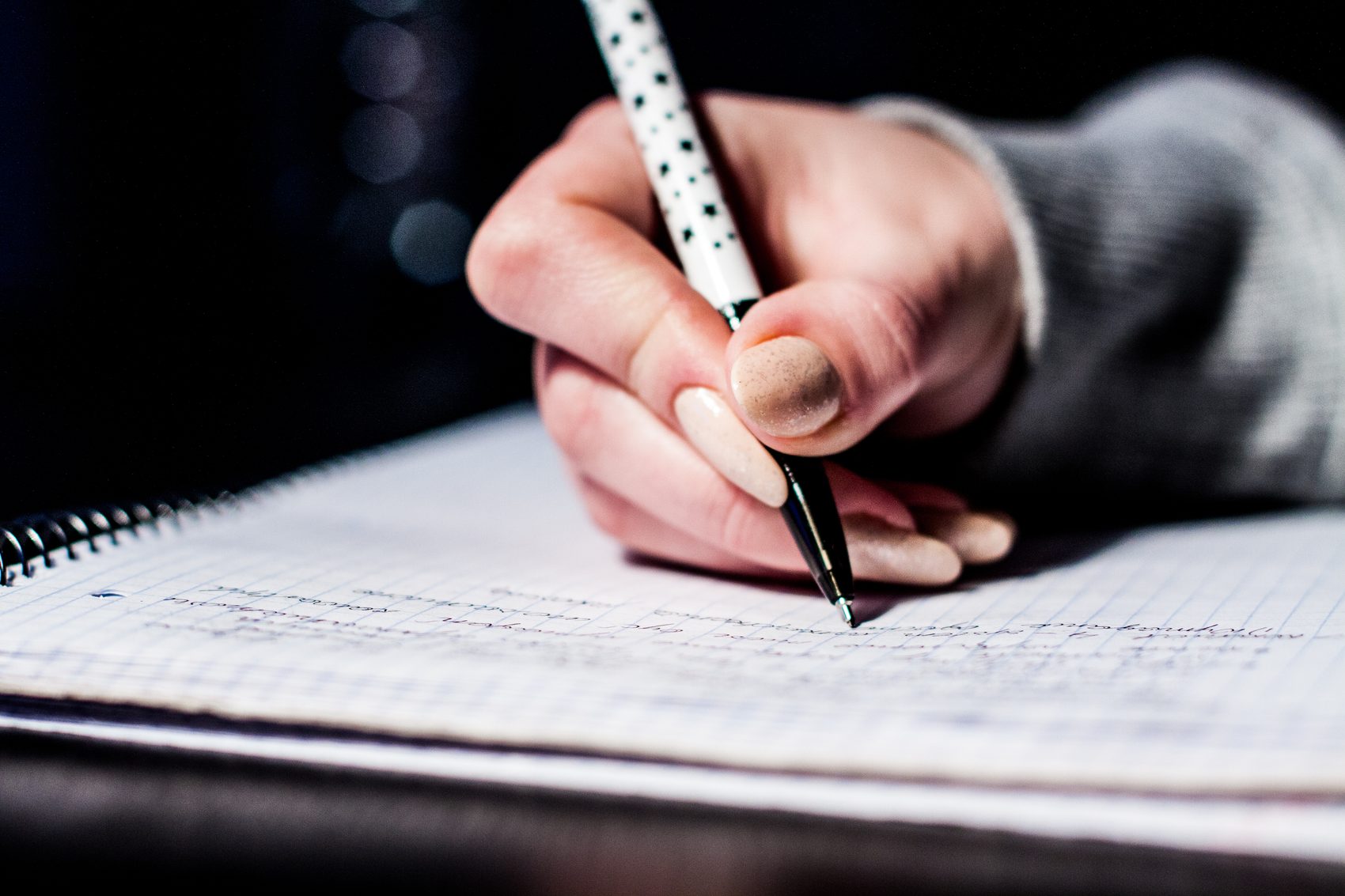 Hand schreibt mit einem Stift in ein kariertes Notizbuch